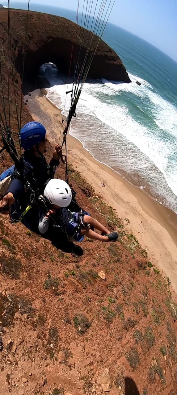 Parapente biplace longeant la falaise rouge et les vagues de l'Atlantique