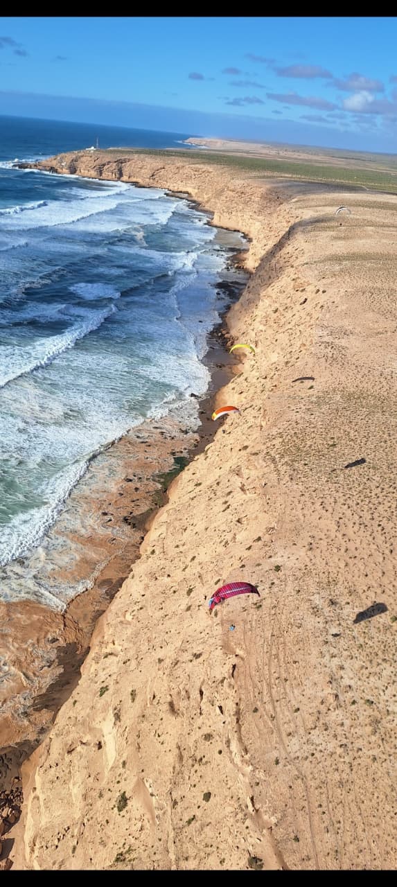 Vue aérienne du littoral sauvage : plage, falaise et parapente au loin